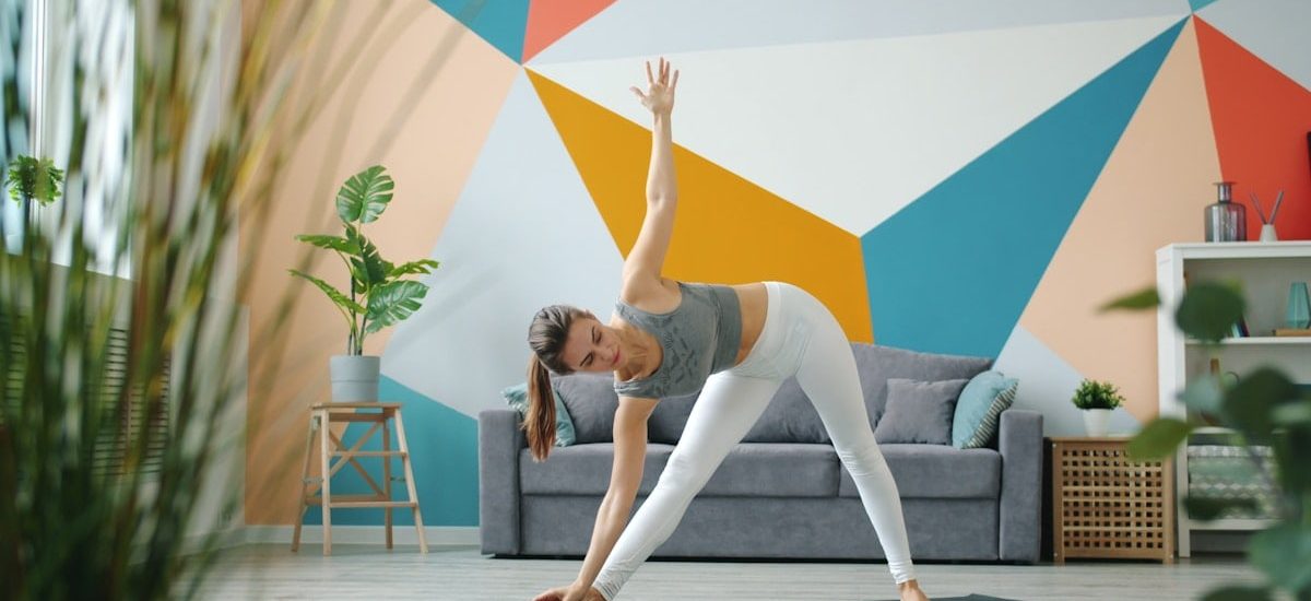 Portrait of cute lady in leggings and top doing yoga at home working out standing on mat exercising. Healthy youth lifestyle and indoor activities concept.
