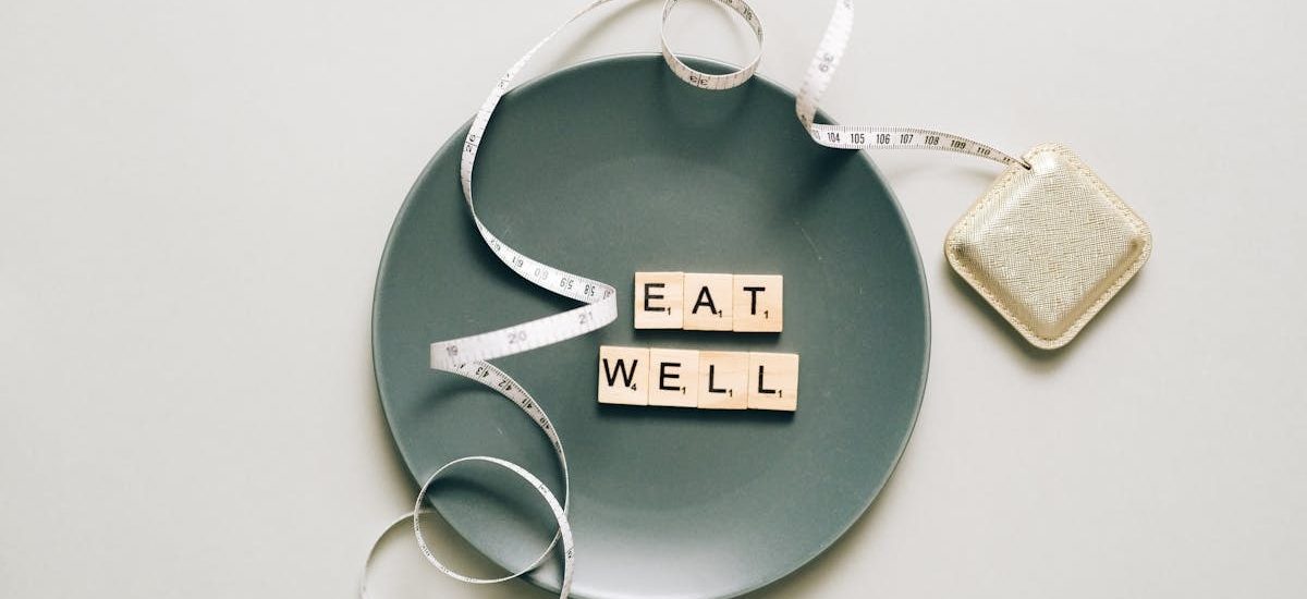 Flat lay of scrabble tiles spelling 'eat well' on a plate with a tape measure, promoting healthy eating.